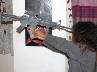 Toveet Radcliffe’s sister demonstrates with a paper gun the angle it would have had to be placed to re-create the shot in her sister’s forehead. (David Sheen)